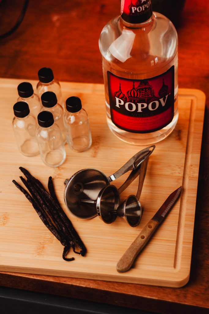 bamboo cutting board with glass bottles, vanilla beans, funnel, paring knife and a bottle of vodka.