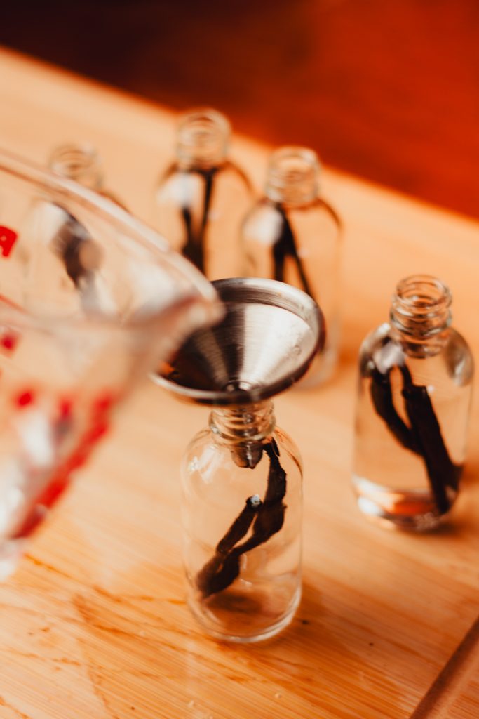 Pouring vodka into bottle with vanilla beans using a stainless steel funnel